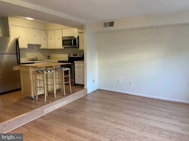 kitchen with appliances with stainless steel finishes, sink, light wood-type flooring, white cabinetry, and a breakfast bar area