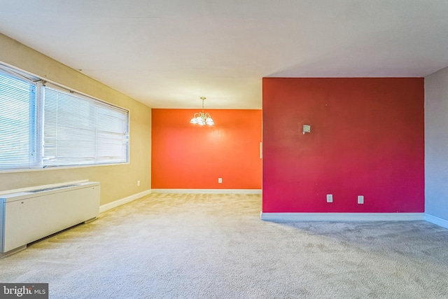 carpeted spare room featuring radiator and a notable chandelier