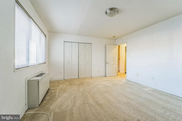 unfurnished bedroom with a closet, light colored carpet, and radiator heating unit