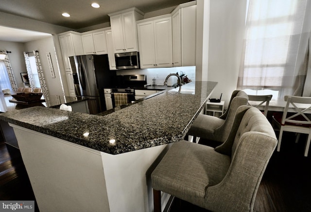 kitchen with a breakfast bar, white cabinets, stainless steel appliances, and dark hardwood / wood-style floors