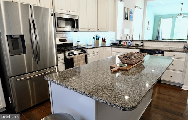 kitchen with kitchen peninsula, white cabinets, dark hardwood / wood-style flooring, appliances with stainless steel finishes, and dark stone counters