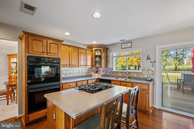 kitchen featuring a kitchen island, sink, black double oven, stainless steel gas cooktop, and dark wood-type flooring