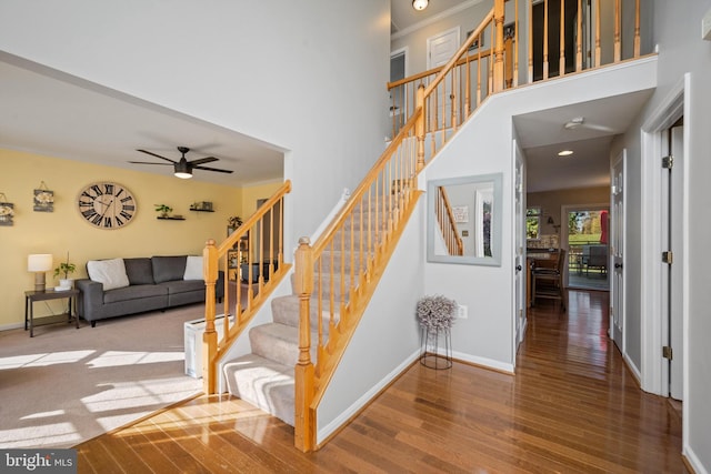 stairs with wood-type flooring, ornamental molding, and ceiling fan