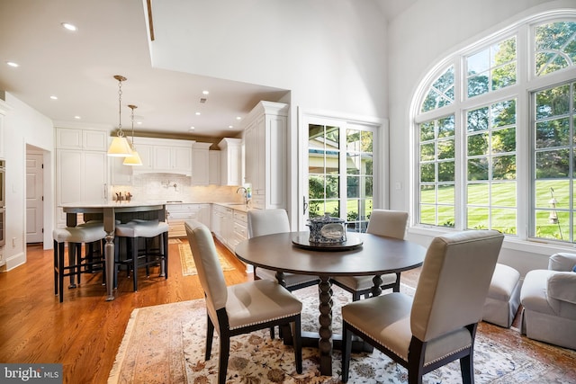 dining area featuring sink, a wealth of natural light, light wood-type flooring, and a high ceiling