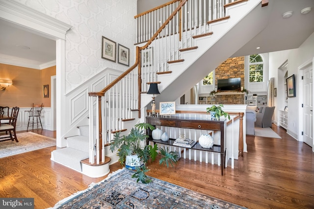 staircase with ornamental molding, hardwood / wood-style floors, a stone fireplace, and a towering ceiling