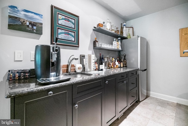 bar featuring sink, dark stone countertops, and stainless steel refrigerator