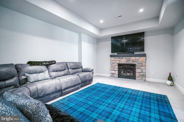 carpeted living room featuring a stone fireplace and a raised ceiling