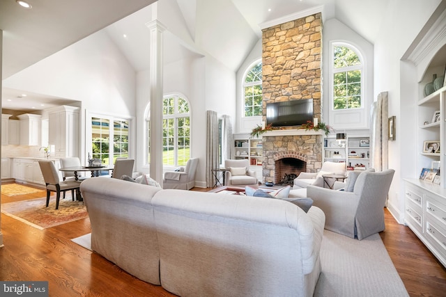 living room featuring hardwood / wood-style flooring, sink, decorative columns, a fireplace, and high vaulted ceiling