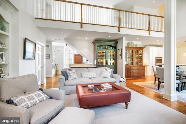 living room featuring decorative columns, built in features, a towering ceiling, and light hardwood / wood-style flooring