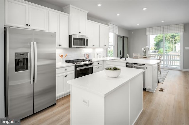 kitchen with appliances with stainless steel finishes, white cabinets, a center island, and a wealth of natural light