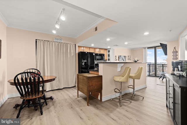 kitchen with a breakfast bar area, black appliances, light hardwood / wood-style flooring, and crown molding