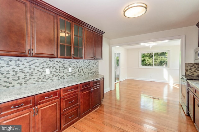 kitchen featuring light stone countertops, stainless steel appliances, decorative backsplash, and light wood-type flooring