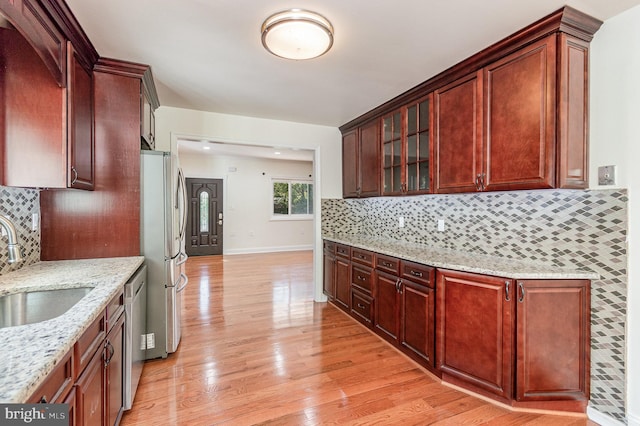 kitchen featuring decorative backsplash, stainless steel appliances, sink, light stone countertops, and light hardwood / wood-style floors