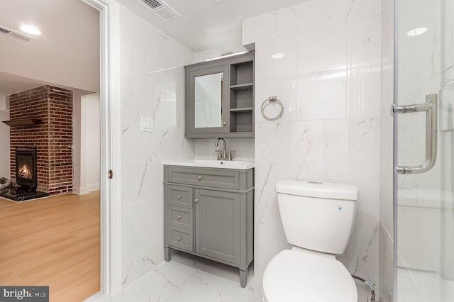 bathroom with toilet, hardwood / wood-style floors, a brick fireplace, vanity, and an enclosed shower