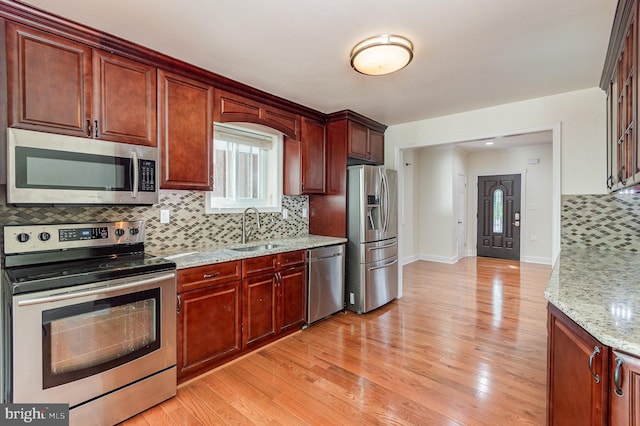 kitchen with tasteful backsplash, stainless steel appliances, sink, and light wood-type flooring