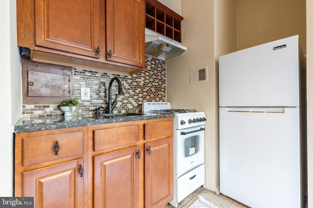 kitchen featuring decorative backsplash, dark stone counters, sink, light tile patterned flooring, and white appliances