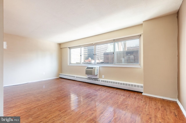 unfurnished room featuring a baseboard heating unit, a wall mounted AC, a textured ceiling, and hardwood / wood-style floors