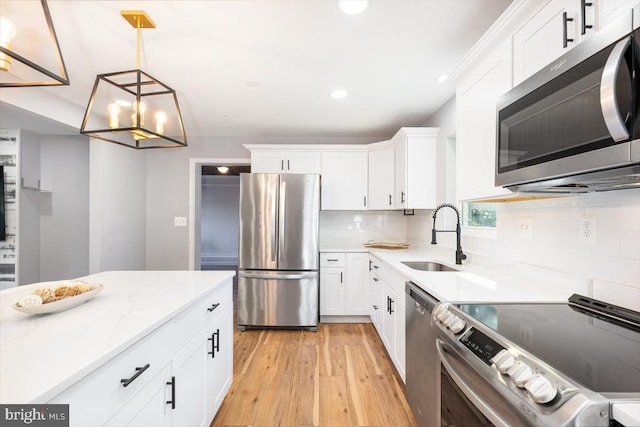 kitchen featuring stainless steel appliances, sink, pendant lighting, white cabinets, and light hardwood / wood-style floors