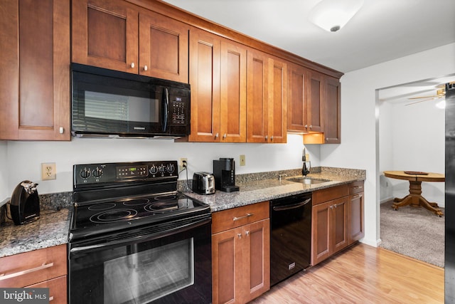 kitchen with light hardwood / wood-style floors, stone counters, black appliances, and sink