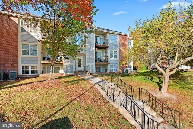 view of front of house featuring a balcony, a front yard, and central air condition unit