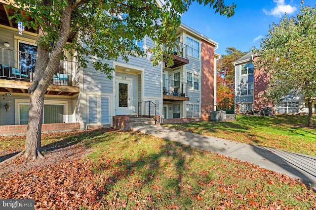 view of front facade with a front yard, a balcony, and central AC unit