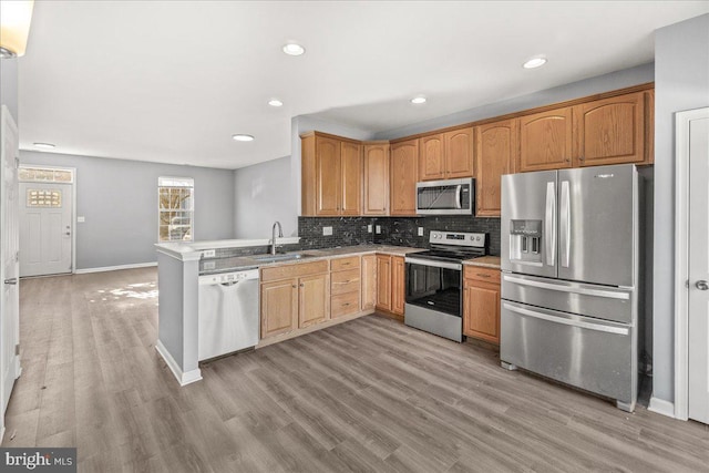 kitchen with kitchen peninsula, sink, stainless steel appliances, and light hardwood / wood-style flooring