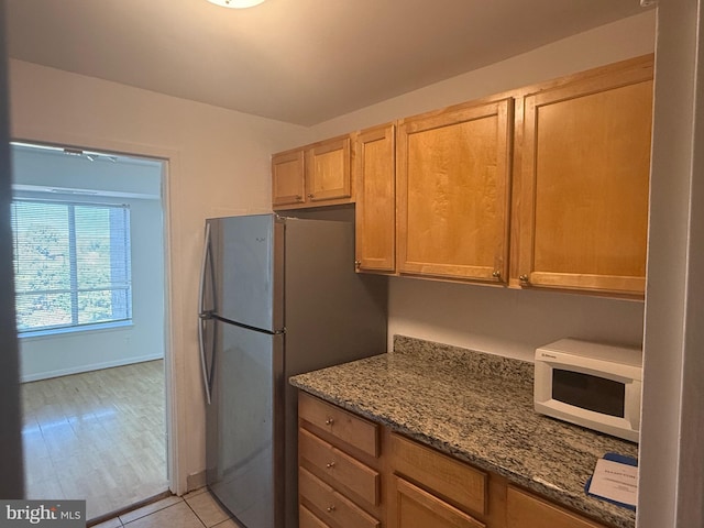 kitchen featuring light hardwood / wood-style floors, stone counters, and stainless steel refrigerator