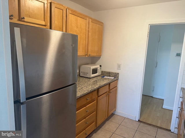 kitchen featuring dark stone countertops, light tile patterned flooring, and stainless steel refrigerator