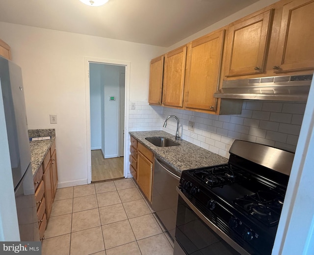 kitchen with decorative backsplash, light tile patterned floors, light stone countertops, sink, and stainless steel appliances