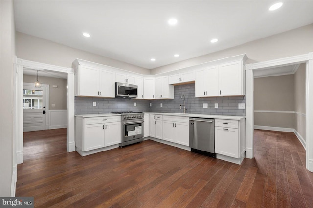 kitchen with appliances with stainless steel finishes, white cabinetry, backsplash, and dark hardwood / wood-style flooring