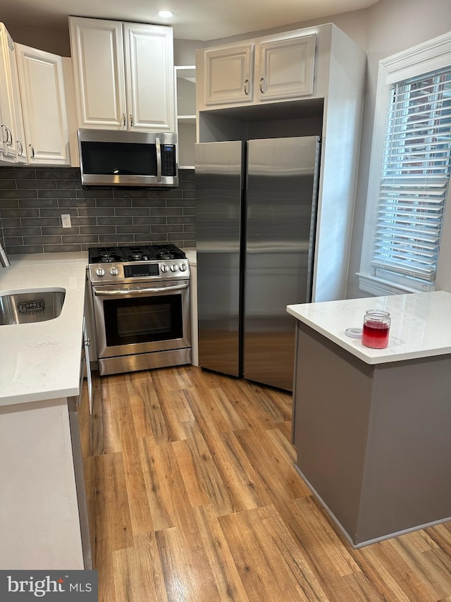 kitchen with decorative backsplash, sink, light wood-type flooring, white cabinetry, and appliances with stainless steel finishes