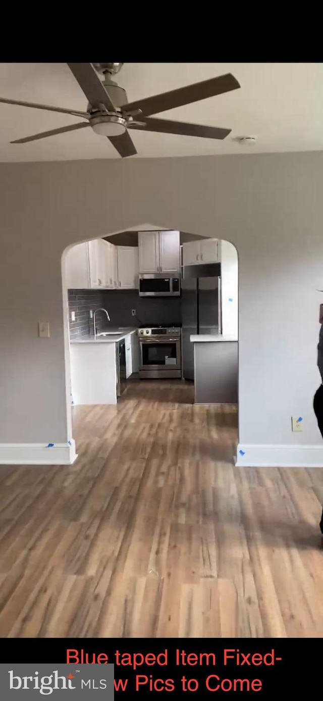 kitchen with appliances with stainless steel finishes, white cabinets, tasteful backsplash, and wood-type flooring