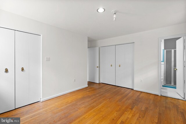 unfurnished bedroom featuring light hardwood / wood-style floors, multiple closets, and ensuite bathroom