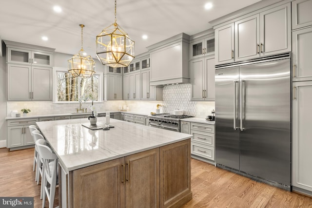 kitchen with custom exhaust hood, a center island, high quality appliances, hanging light fixtures, and light stone countertops