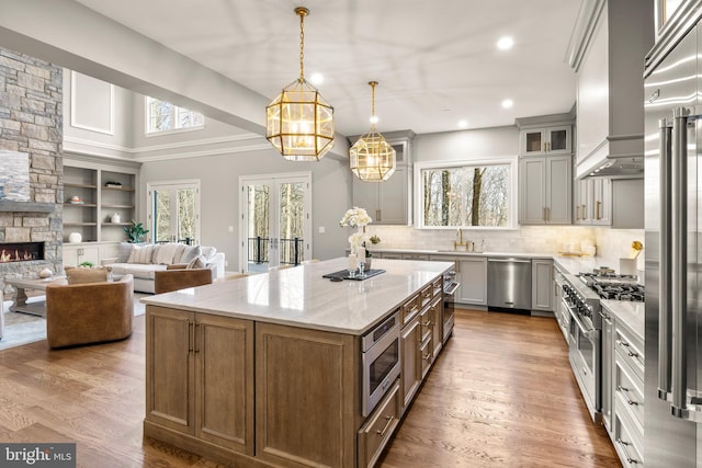 kitchen featuring built in appliances, light stone countertops, hardwood / wood-style floors, and hanging light fixtures