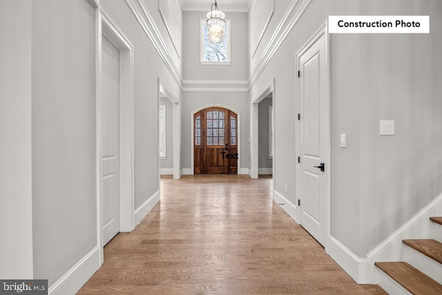 entryway featuring light wood-type flooring, crown molding, a towering ceiling, and an inviting chandelier