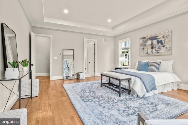 bedroom with a tray ceiling, ornamental molding, and light wood-type flooring