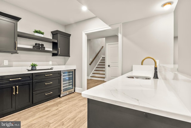 kitchen with light wood-type flooring, light stone counters, wine cooler, and sink