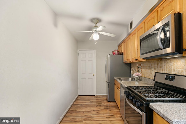 kitchen featuring decorative backsplash, ceiling fan, appliances with stainless steel finishes, light wood-type flooring, and sink