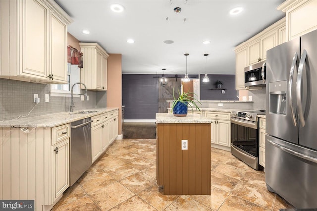 kitchen featuring hanging light fixtures, appliances with stainless steel finishes, light stone countertops, cream cabinetry, and a center island