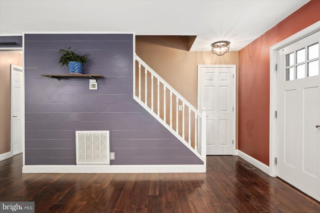 foyer featuring dark wood-type flooring, wood walls, and an inviting chandelier