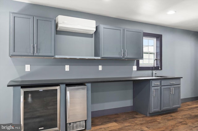 kitchen with gray cabinetry, sink, a wall mounted air conditioner, beverage cooler, and dark wood-type flooring