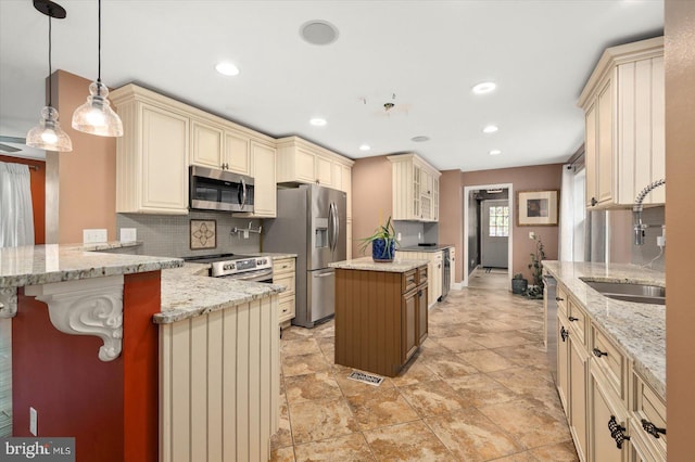 kitchen with cream cabinets, a kitchen breakfast bar, stainless steel appliances, decorative light fixtures, and a center island