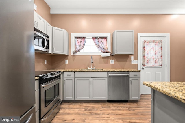 kitchen featuring appliances with stainless steel finishes, light stone countertops, sink, and light wood-type flooring