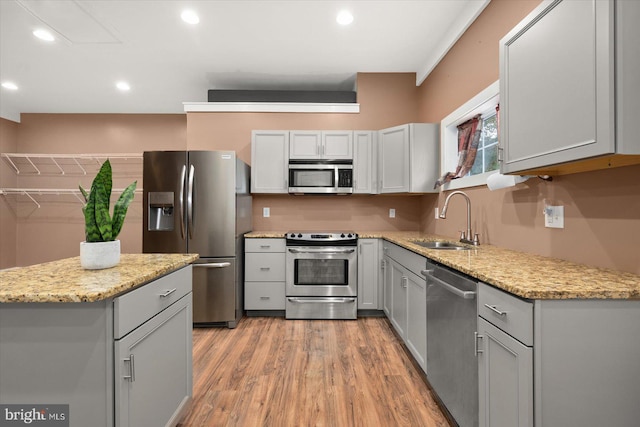 kitchen with stainless steel appliances, sink, gray cabinets, light stone counters, and light hardwood / wood-style floors