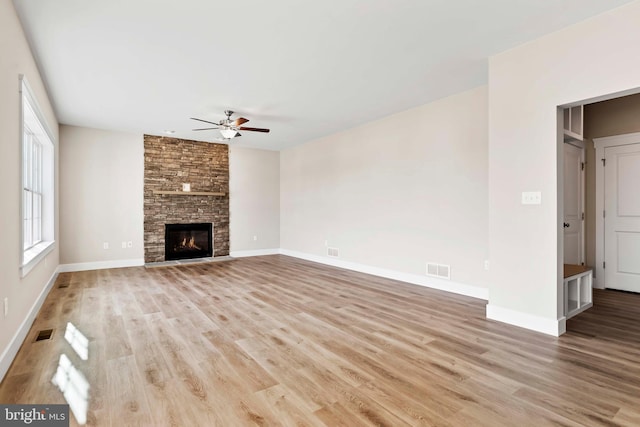 unfurnished living room featuring a stone fireplace, wood finished floors, ceiling fan, baseboards, and visible vents