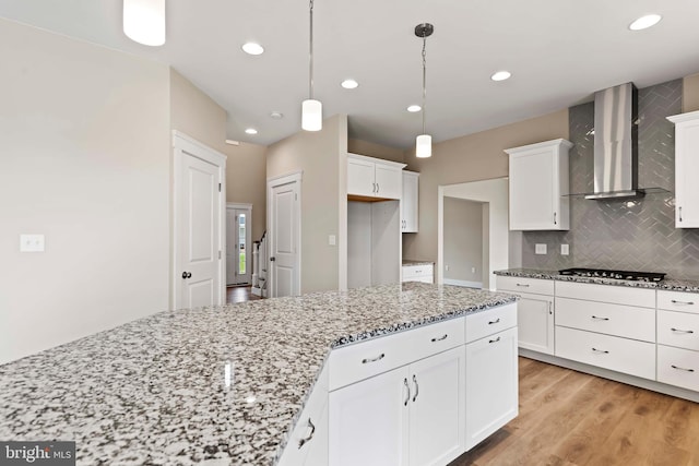 kitchen with wall chimney exhaust hood, pendant lighting, stainless steel gas stovetop, white cabinetry, and light hardwood / wood-style floors