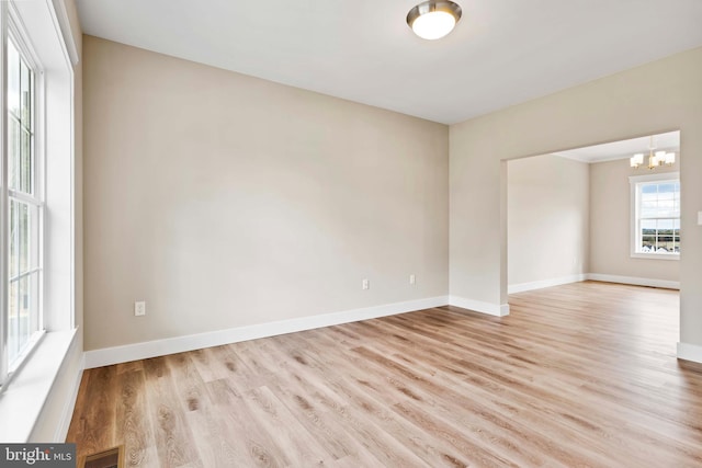 empty room with baseboards, wood finished floors, visible vents, and an inviting chandelier