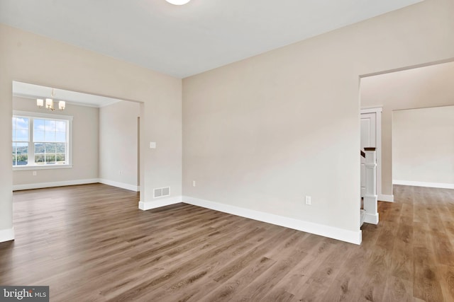 unfurnished room with wood finished floors, visible vents, baseboards, and an inviting chandelier