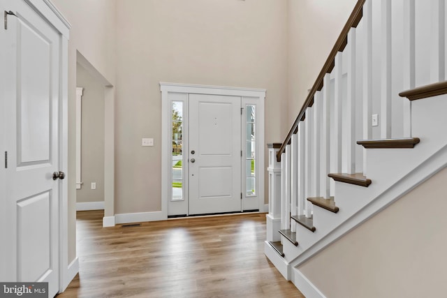 foyer entrance with baseboards, wood finished floors, a towering ceiling, and stairs
